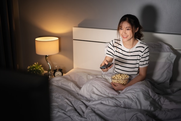 Happy young woman watching TV on a bed at night