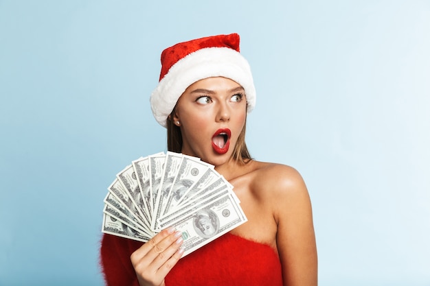 クリスマスの帽子をかぶって、お金を持って幸せな若い女性。