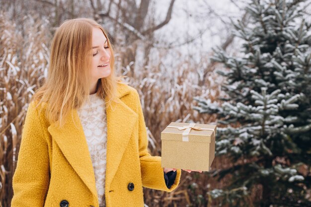 Happy young woman wearing a coat holding a Christmas present box over nature