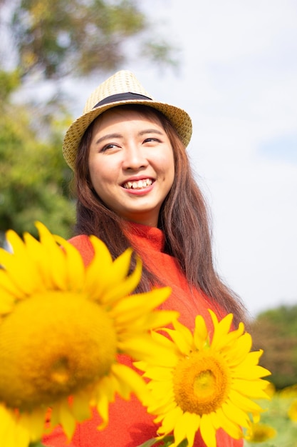 Happy young woman wearing hat while standing by sunflowers against sky