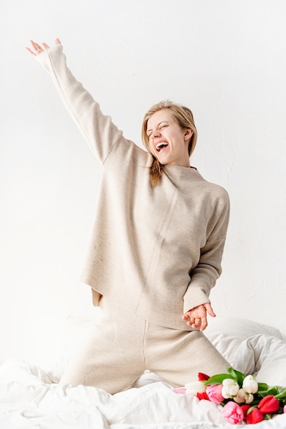 Happy young woman wearing pajamas dancing on the bed having fun