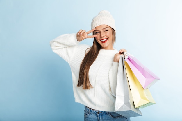Happy young woman wearing sweater, carrying shopping bags, showing peace gesture
