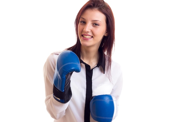 Happy young woman in white shirt with dark hair and blue boxing gloves on white background in studio