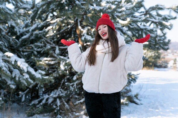 Happy young woman in winter in forest. Brunette girl in red hat smiling and enjoy the winter.