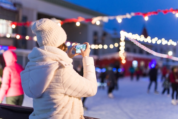 アイスリンクで冬の幸せな若い女性がスマートフォンのselfieで写真を撮る