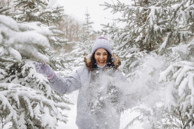 Happy young woman in winter on a walk in nature. a woman in a lilac jacket stands near the Christmas trees in a winter park.