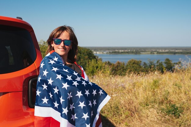 차 근처 자연에서 미국 국기와 함께 행복 한 젊은 여자