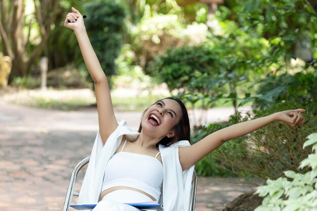 写真 公園の席に座って腕を伸ばした幸せな若い女性