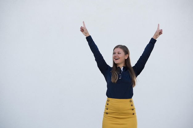 Happy young woman with arms raised standing against gray background