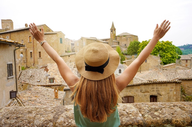 Felice giovane donna con le braccia in alto nella città di orvieto ragazza viaggiatore con le braccia tese sollevate sulla città turista in vacanza in viaggio nel centro italia