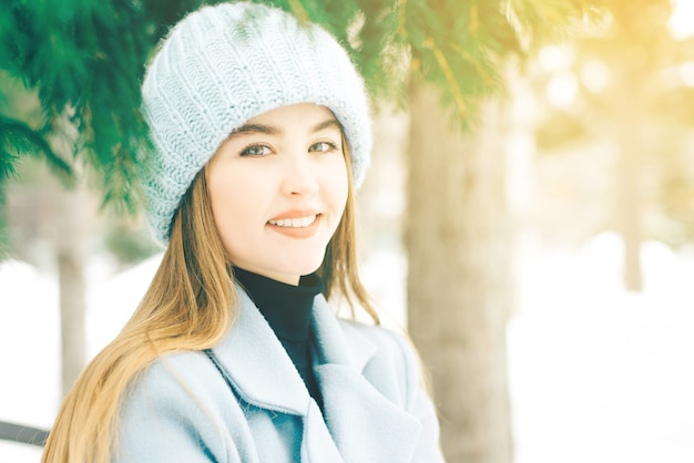 Giovane donna felice con i bei occhi azzurri con trucco naturale in un sorriso dolce in un cappello tricottato in un cappotto blu su all'aperto.