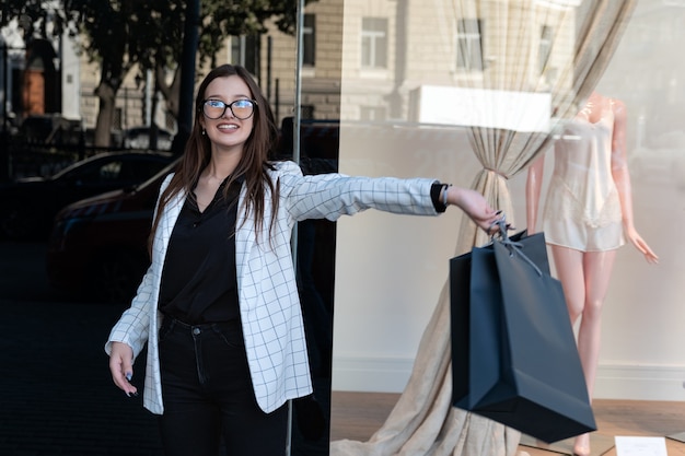 Happy young woman with black shopping bag on shop window background. Girl student after shopping with bag in her hands.