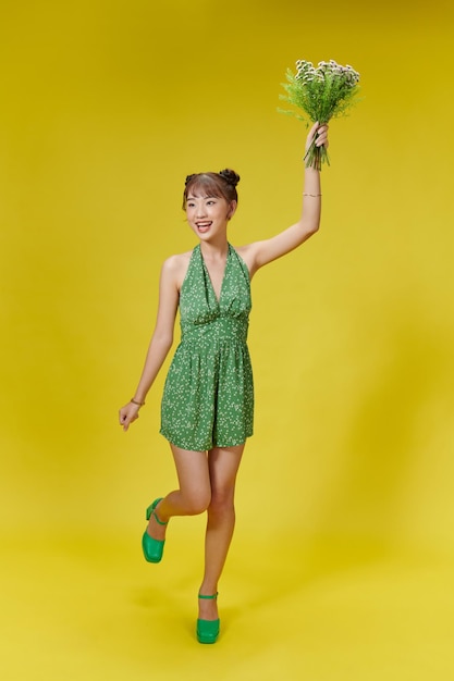 Happy young woman with bouquet of flowers isolated over yellow background