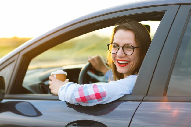 Happy young woman with coffee to go driving her car