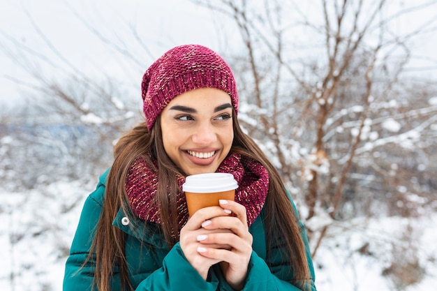 暖かい服を着て使い捨てのコーヒーやお茶と幸せな若い女性。