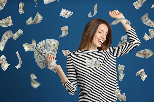 青の背景にお金の雨の下でドルを持つ幸せな若い女