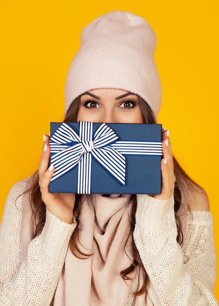 Happy young woman with a gift box in her hands covers half of h