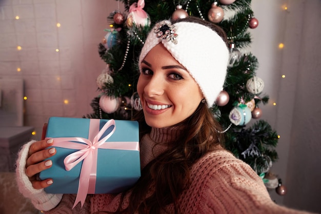 A happy young woman with a gift in her hand takes selfies against the Christmas tree Merry Christmas