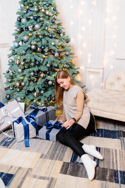 Happy young woman with a gift lying near the Christmas tree White silver color on sofa background Merry Christmas and New Year Atmospheric moments