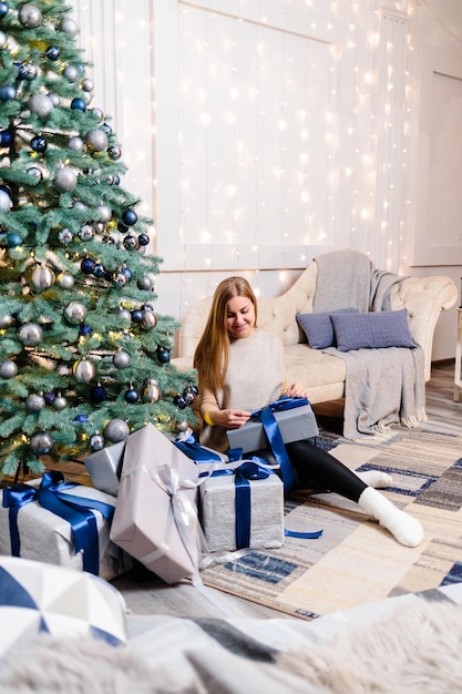 クリスマス ツリーのそばに横たわっている贈り物を持つ幸せな若い女性 ソファの背景に白い銀色 メリー クリスマスと新年の大気の瞬間