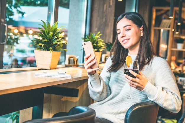 Happy young woman with glass of wine checking the phone