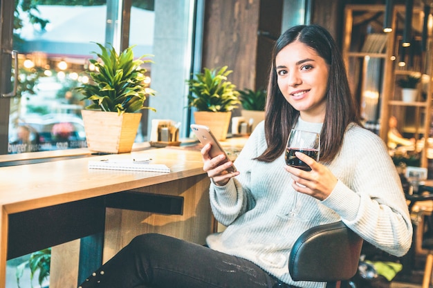 Счастливая молодая женщина с бокалом вина или глинтвейн, проверка телефона
