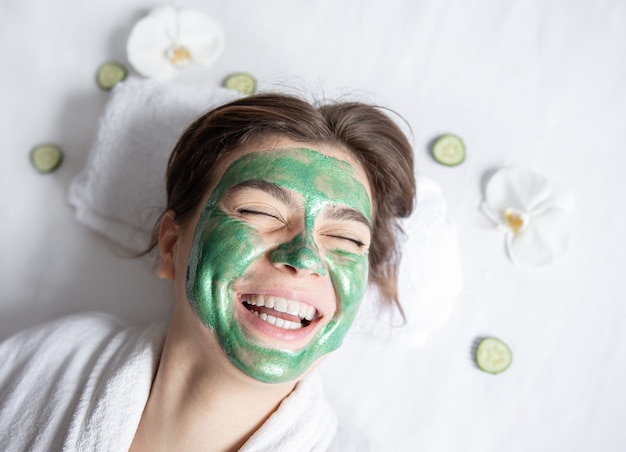 Happy young woman with a green cosmetic mask on her face top view