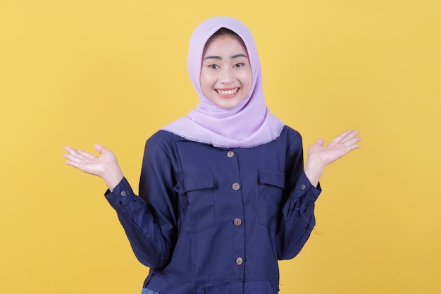 사진 행복한 표정을 가진 행복한 젊은 여성은 노란색으로 히잡과 평상복을 입은 그녀의 손에 뭔가를 보여줍니다