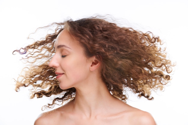 Happy young woman with healthy skin whirling her head with dark long wavy hair while drying it after washing with hydrating shampoo