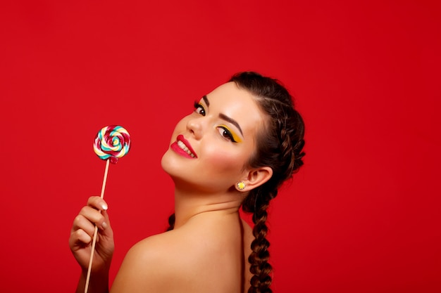 Happy young woman with lollipop, red against a red wall