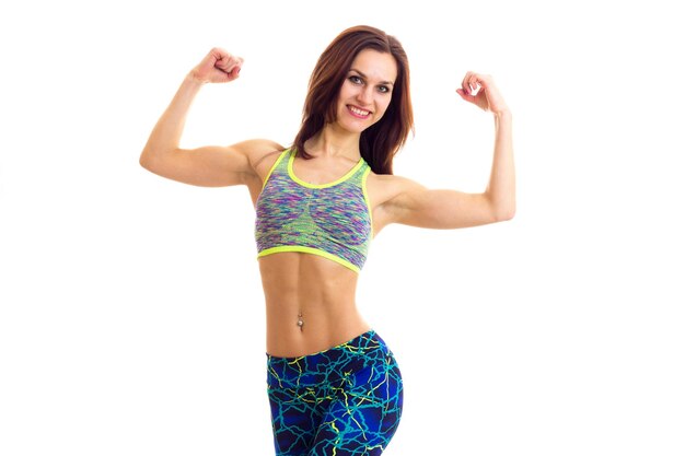 Happy young woman with long brown hair wearing in colored sports top and leggins showing her biceps