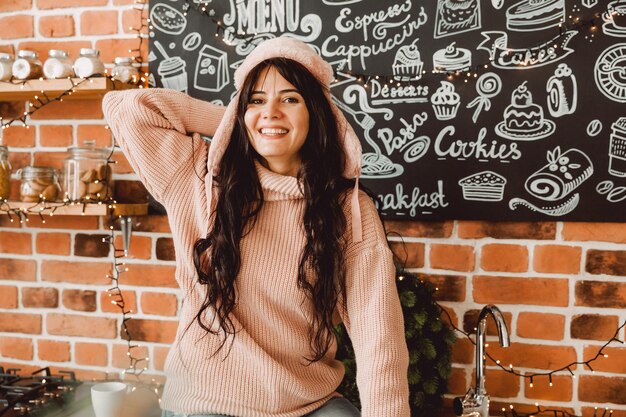 Happy young woman with long hair and in a winter fur hat drinks coffee sitting in the kitchen at home. christmas concept.