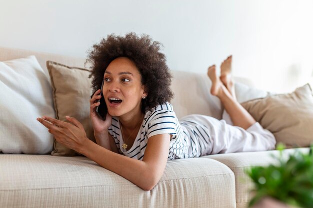 Happy young woman with mobile phone laying on sofa Beautiful young black women using tablet computer