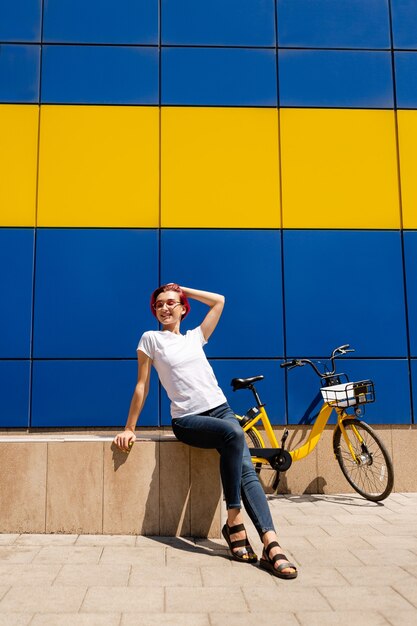 Happy young woman with pink hair walks around the city on a bike in the summer