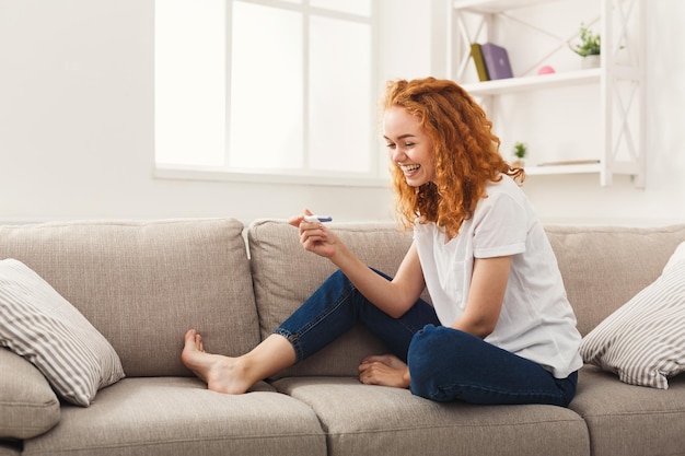 Happy young woman with pregnancy test at home. Expectation, pregnancy, maternity and family issues concept