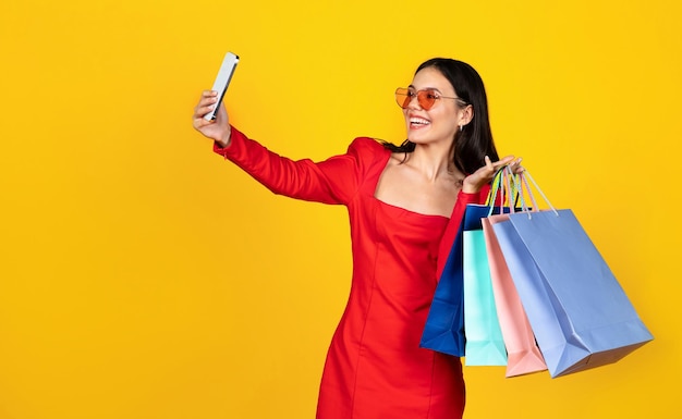 Happy young woman with shopping bags taking selfie on smartphone