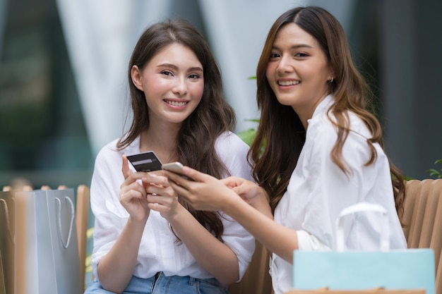 Happy young woman with smiley face talking and laughing holding credit card and using phone