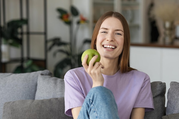 写真 カメラを見ている青リンゴを持って真っ白な笑顔で幸せな若い女性。健康的なライフスタイルのコンセプト