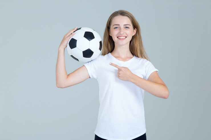 彼女の手でサッカーボールを持つ幸せな若い女性は灰色の側を指す