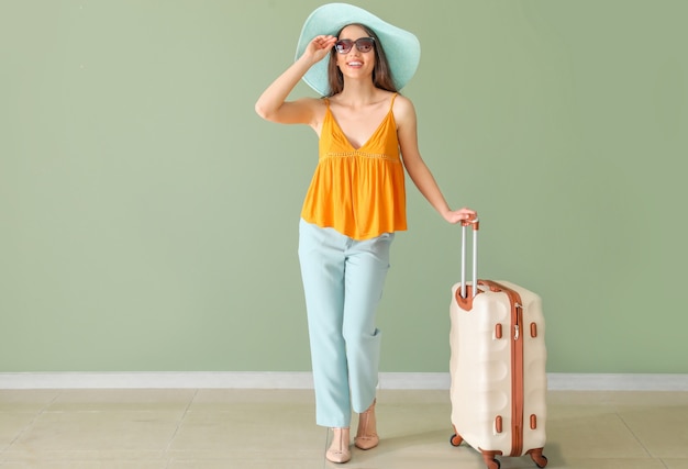 Happy young woman with suitcase near color wall