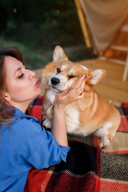 Welsh Corgi Pembroke 개와 함께 여름날 글램핑에서 휴식을 취하는 행복한 젊은 여성 야외 레크리에이션 및 레크리에이션 라이프스타일 컨셉을 위한 럭셔리 캠핑 텐트