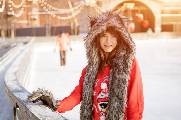 Giovane donna felice in un cappello di lupo in inverno presso la pista di pattinaggio