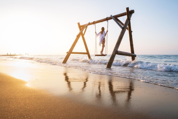 Happy young woman on wooden swing in water beautiful blue sea