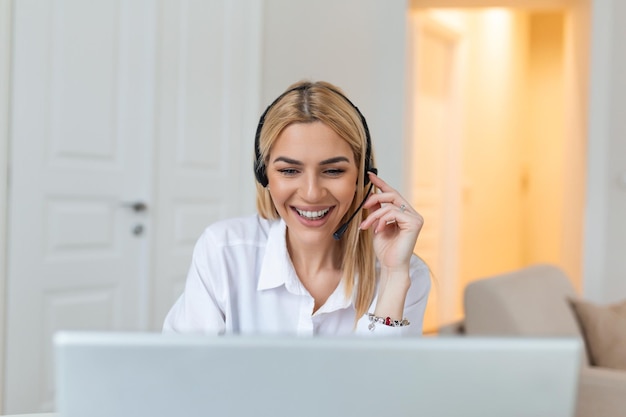 Happy young woman working on laptop while talking to customer on phone Consulting corporate client in conversation with customer using computer Service desk consultant talking in a call center