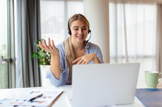 Happy young woman working on laptop while talking to customer\
on phone consulting corporate client in conversation with customer\
using computer service desk consultant talking in a call\
center