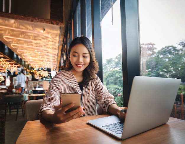 happy young woman working remotely at a coffee shop using her mobile phone and laptop enjoying the freedom of freelance work