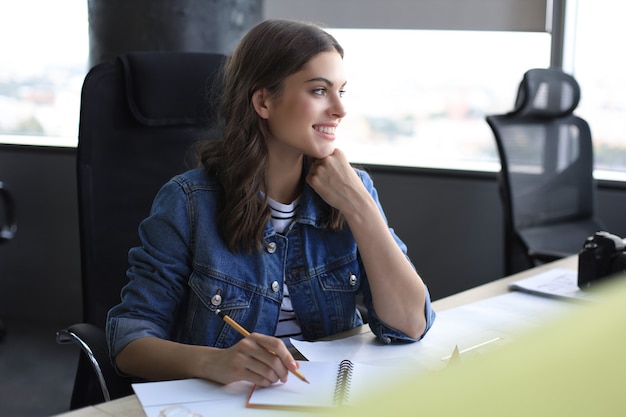 Happy young woman writing something down while working in the office.