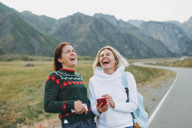Photo happy young women travellers using mobile on road against the beautiful mountain landscape