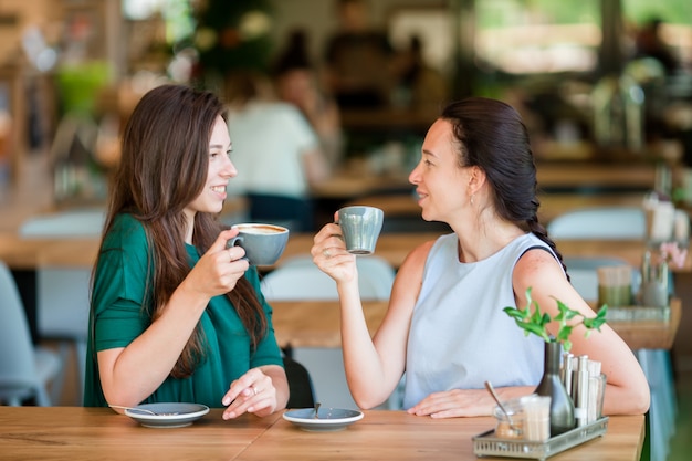 Счастливые молодые женщины с чашками кофе в кафе на открытом воздухе. Концепция общения и дружбы