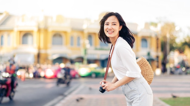 カメラを持った幸せな若者のアジア人女性は、週末の余暇に通りの街を旅します。